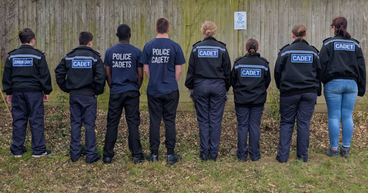 Eight police cadets in front of the nascent Hathaway Court hedgerow, facing away from the camera to show the "CADET" markings on their uniforms