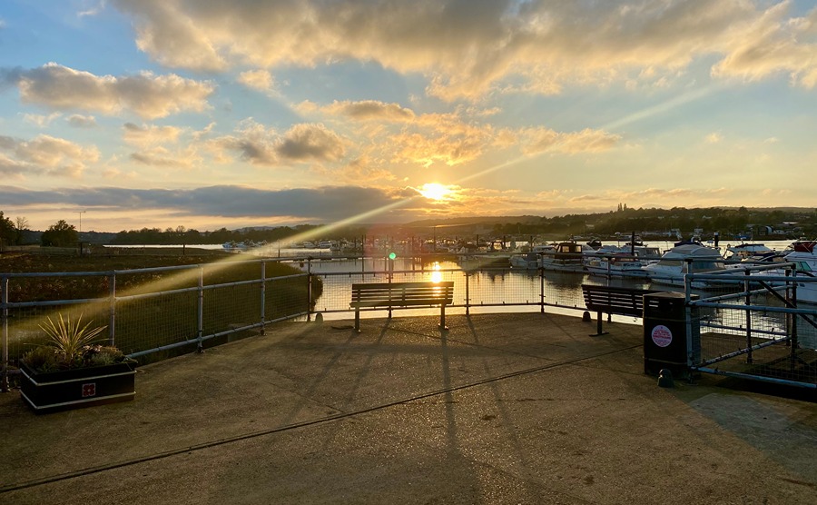 A view of the sun setting over the River Medway taken from Rochester Pier, with the pier's planters and benches visible, as well as moored boats