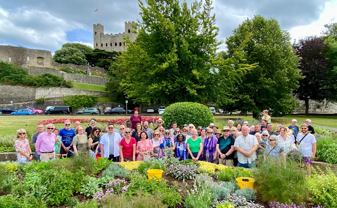 A large group of supporters posing amid the sensory garden with trees and Rochester Castle keep in the background