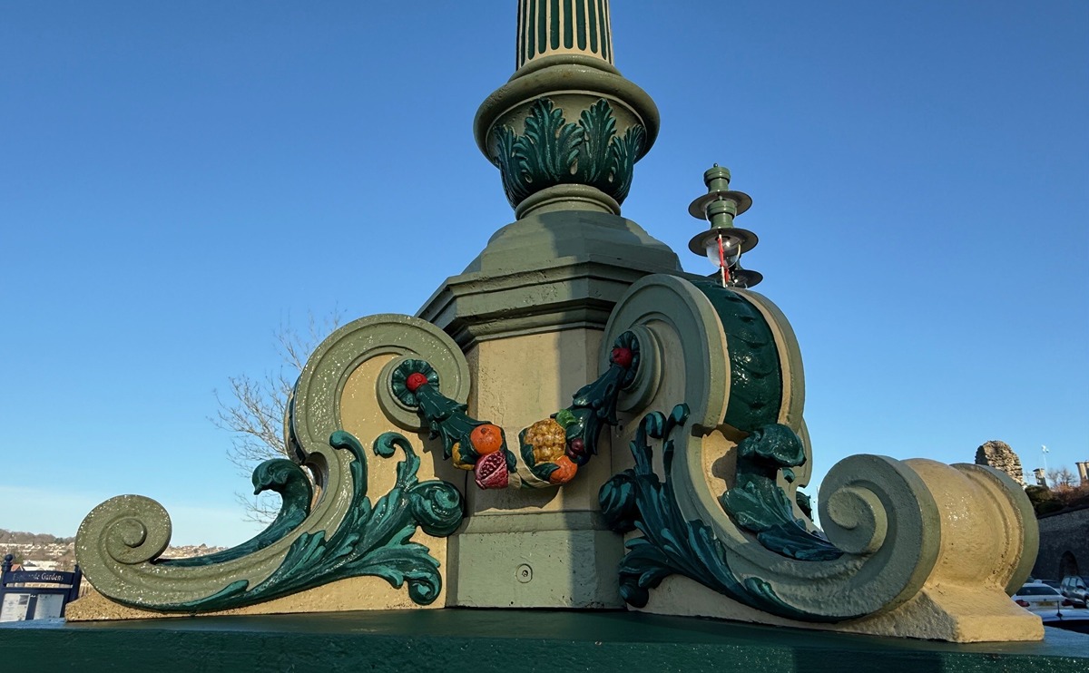 The pedestal columns of ornate cast iron lamps, with elegant scrollwork and fruit and leaf motifs, painted cast iron