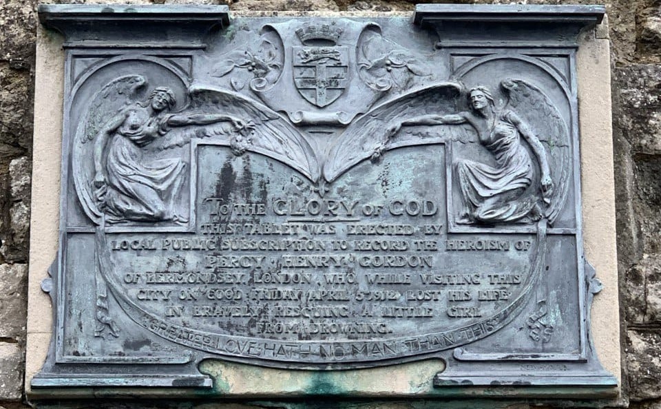 A bronze plaque adorned with angels and reading "TO THE GLORY OF GOD - THIS TABLET WAS ERECTED BY LOCAL PUBLIC SUBSCRIPTION TO RECORD THE HEROISM OF PERCY HENRY GORDON OF BERMONDSEY, LONDON, WHO WHILE VISITING THIS CITY ON GOOD FRIDAY APRIL 5th 1912 LOST HIS LIFE IN BRAVELY RESCUING A LITTLE GIRL FROM DROWNING - GREATER LOVE HATH NO MAN THAN THIS"